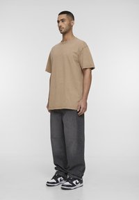 Camiseta oversized en algodón de manga corta, combinada con unos pantalones vaqueros grises holgados y zapatillas negras y blancas. Diseño simple y relajado.