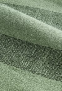 Tissu tissé vert clair et vert foncé avec de larges rayures horizontales et une surface texturée, montré en gros plan.