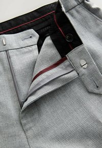 Pantaloni grigi con trama, chiusura con cerniera, fodera della cintura nera e dettagli in bordeaux e grigio. Presentano una chiusura con bottone e gancio.