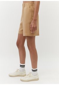 Bruna shorts med elastisk midjeband, sidfickor och avslappnad passform, matchade med vita sneakers och randiga strumpor.