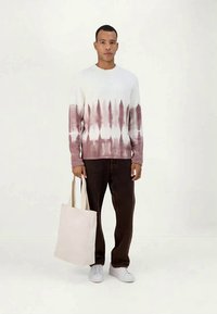 White and burgundy tie-dye sweater, round neck, long sleeves, paired with dark brown pants and a cream canvas tote bag. White sneakers.