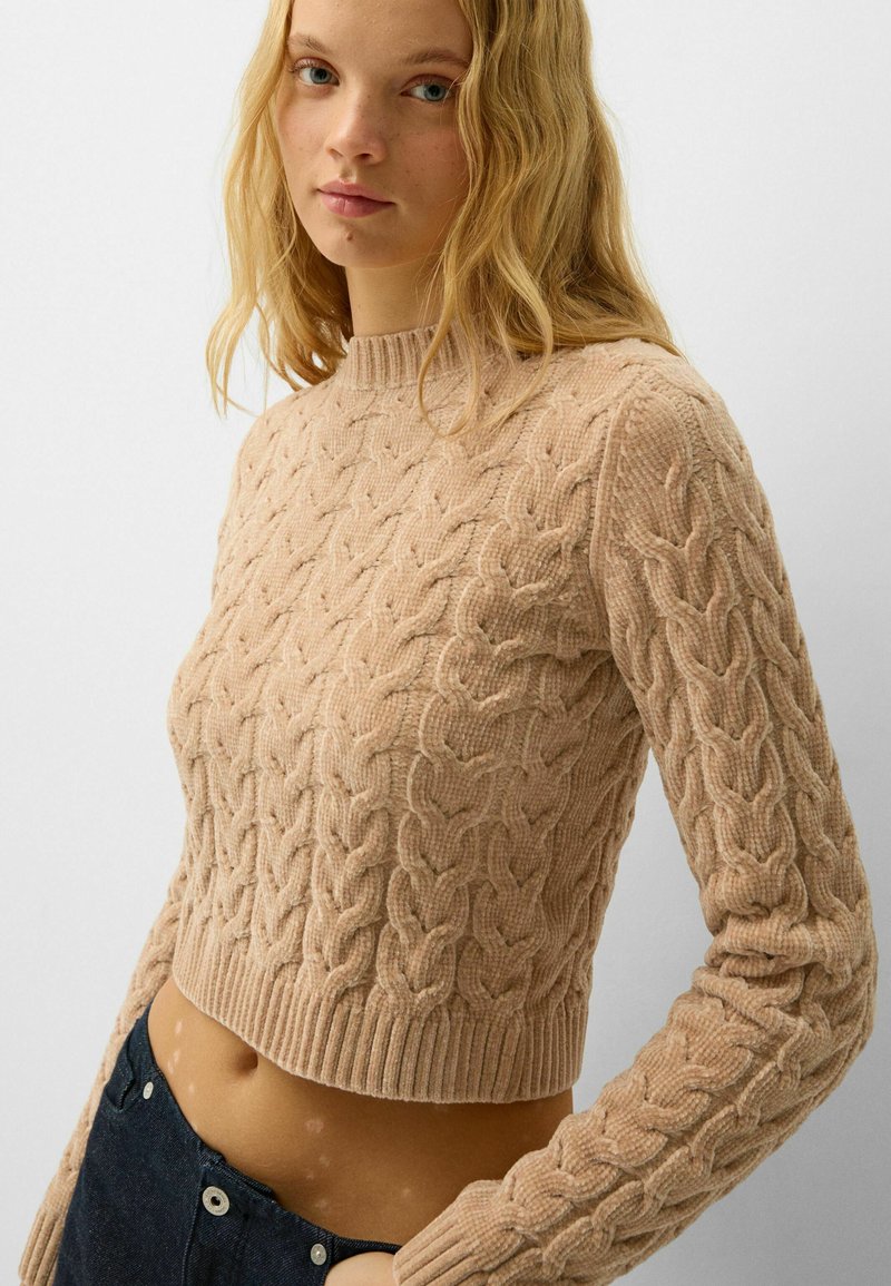 Maglione beige a maglia rasata con collo rotondo, polsini e orlo a costine. Presenta motivi testurizzati e un design cropped.