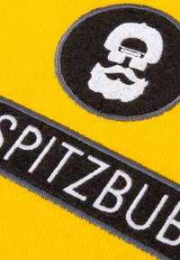 Yellow fabric with a black logo featuring a skull and beard, bordered by a dark patch labeled "SPITZBUB." Textured embroidery details.