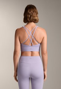 Lila športna modrček z obrnjenimi naramnicami in gladko teksturo, v kombinaciji z usklajenimi legginsami z visokim pasom.