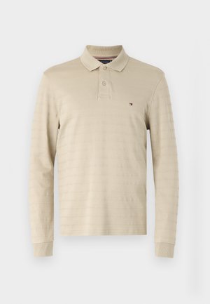 Beige langærmet polo shirt lavet af tekstureret stof, med krave, tre knapper og et lille, broderet logo på brystet.