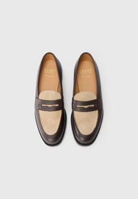 Mörkbruna läderloafers med ljusbeige mockatopp, guldmärkta innersulor och en slip-on design, uppvisade mot en ljusgrå bakgrund.