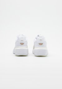 Paire de baskets Nike blanches vues de dos avec des détails perforés et de petits logos Swoosh orange au-dessus des talons.