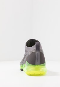 Nike VaporMax sneakers z szarym, dzianinowym wierzchem, czarnym akcentem przy pięcie i przezroczystą gumową podeszwą w jasnym zielonym kolorze. Gładka tekstura w całej konstrukcji.