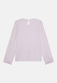 Maglietta lunga di colore lilla realizzata in tessuto morbido. Presenta un'apertura a chiave sul retro e polsini elasticizzati con un bordo in pizzo.