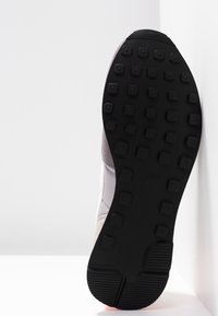 Semelle d'une basket avec une semelle extérieure en caoutchouc noir comportant des crampons carrés pour la traction, positionnée sur un fond blanc.