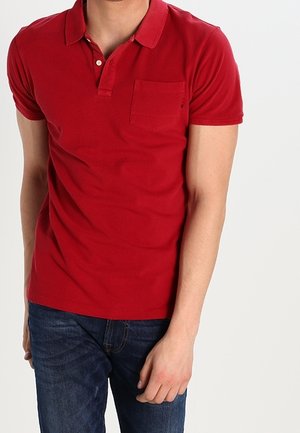 Rød bomulds polo skjorte med krave, korte ærmer og en brystlomme. Båret sammen med mørkeblå denim jeans.