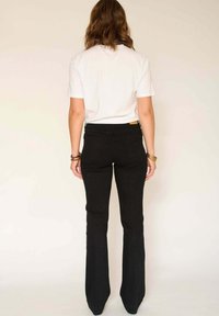 Jean flare noir taille haute, texture lisse, avec des détails de couture subtils, associé à un t-shirt blanc à manches courtes.