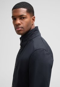 Navy blue jacket with a high collar, featuring classic button closure, smooth texture, and tailored fit. Subtle stitching details visible.