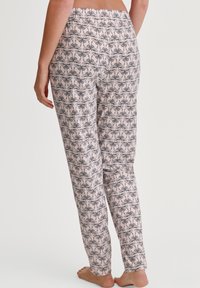 Lichtroze pyjamabroek met een zwart bloemenpatroon, elastische tailleband, rechte pijpen en een gladde structuur. Ontwerp zichtbaar van achteren.