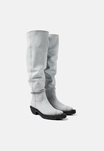 Botas de tela gris hasta la rodilla con un diseño holgado. Presentan costuras contrastantes y una suela de goma negra texturizada.