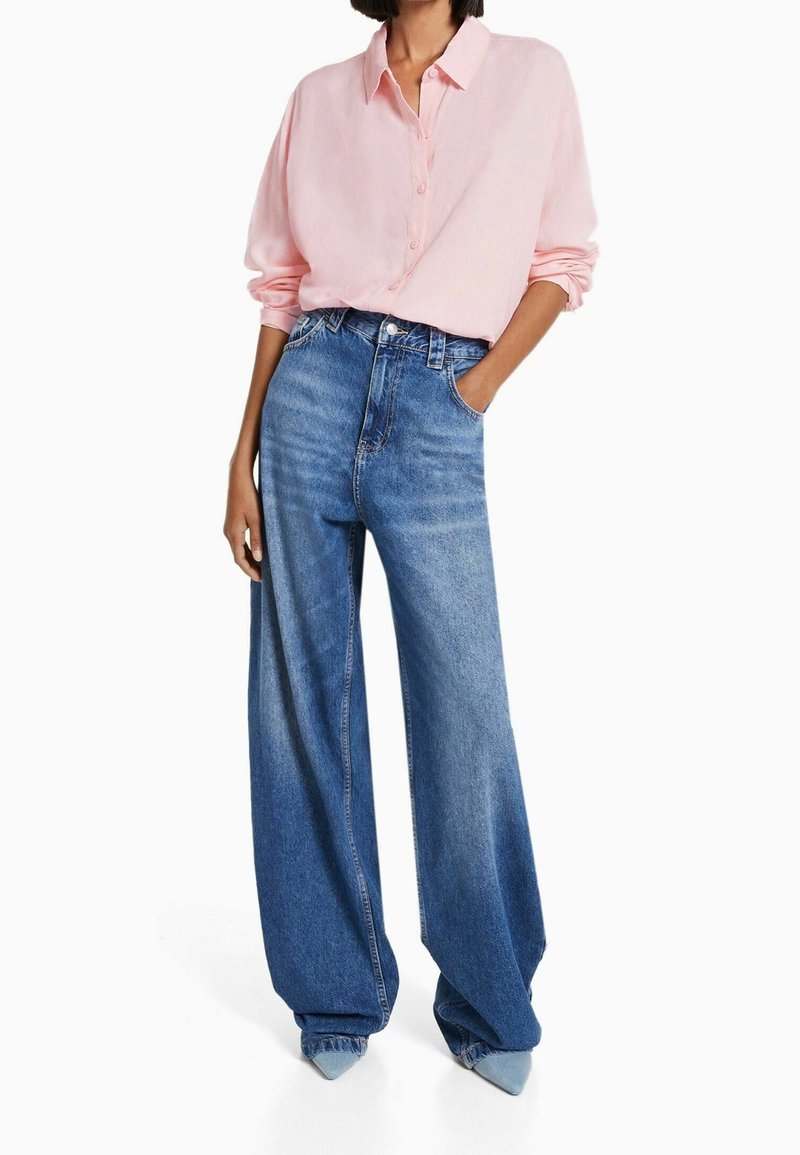 Light pink, long-sleeve button-up shirt paired with wide-leg, high-waisted blue denim jeans; smooth fabric and relaxed fit with pockets.