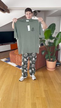 Grågrøn t-shirt med rund hals og korte ærmer, der har et trykt logo. Sammen med mønstrede pyjamabukser i mørkegrøn og hvid.