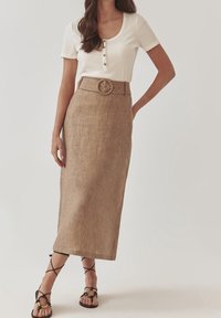 Biała, prążkowana bluzka z krótkim rękawem z guzikami zestawiona z beżową, lnianą spódnicą o wysokim stanie z dużą klamrą i prostym krojem. Czarne sandały.
