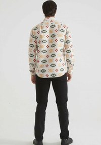 Chemise à manches longues en tissu blanc avec un motif géométrique multicolore, présentant des motifs verts, rouges et orange, et un col boutonné.