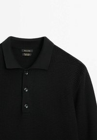 Polo noir avec un motif tissé texturé, doté d'un col plat et de trois boutons ronds au niveau du cou.