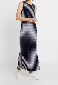 Robe maxi à rayures bleu marine et blanches, sans manches, avec des fentes latérales et une texture douce, portée avec des baskets plateformes blanches.