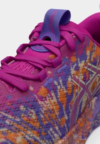 Μωβ παπούτσι για τρέξιμο με υφή και σχέδιο στο επάνω μέρος, που περιλαμβάνει ροζ, πορτοκαλί και μπλε λεπτομέρειες. Διαθέτει κορδόνια και μια ετικέτα έλξης με το λογότυπο στη φτέρνα.