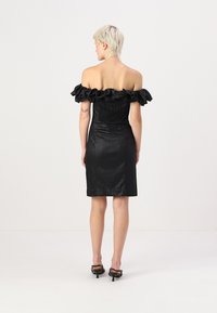 Μαύρο φόρεμα χωρίς τιράντες με ρυτιδωμένο λαιμό, εφαρμοστό σχήμα και υφή υφάσματος, πέφτει λίγο πάνω από το γόνατο. Μαύρα τακούνια.