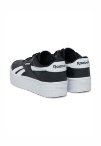 Juodos Reebok sportbačiai su baltais akcentais, turintys lygų sintetinio audinio viršų, su raištelių uždarymu ir tekstūruotu baltu platforminiu padu.