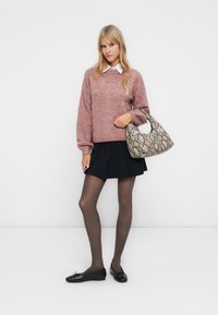 Maglione rosa lavorato a maglia con motivo testurizzato, gonna nera plissettata, ballerine nere e borsa con stampa pitone, su uno sfondo chiaro.