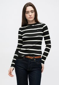 Mustvalgete triipudega pikad varrukad, soonilise tekstuuriga, ümar kaelus ja väikese logoga rinnal, kombineeritud tume teksadega.