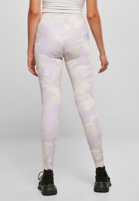 Leggings camo lavande en tissu extensible avec une taille haute, présentant une texture lisse et une coupe fuselée. Bottines noires visibles.
