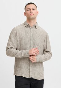 Lett, mønstret skjorte i beige med subtile striber. Har krave, lange ærmer og en brystlomme. Blød tekstur.