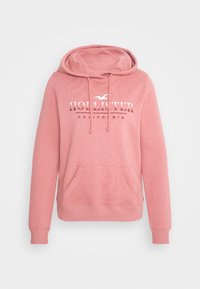Rosa hoodie i mjukt tyg, med en framficka, ribbade manschetter och en huva med dragsko. "Hollister California"-loggan tryckt i vitt.
