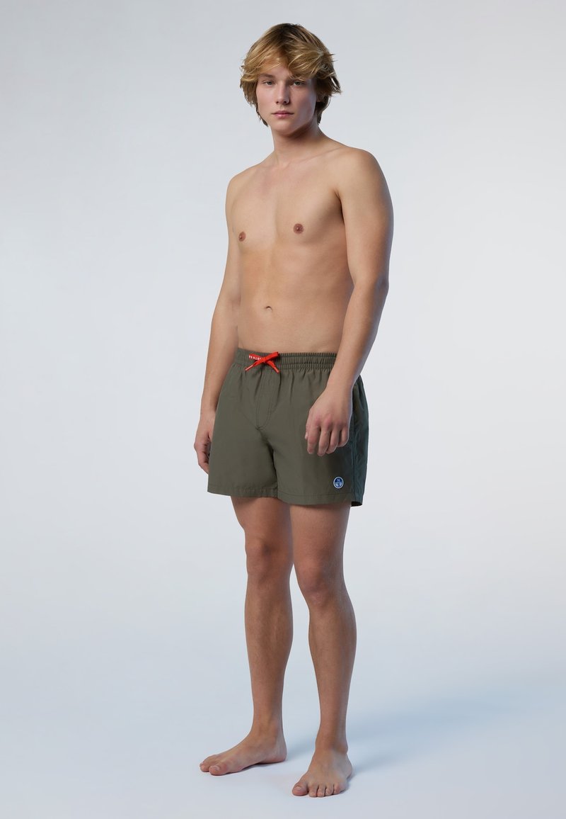 Costumi da bagno verde oliva scuro con cintura elastica e cordino rosso, caratterizzati da un piccolo logo blu sulla gamba sinistra.