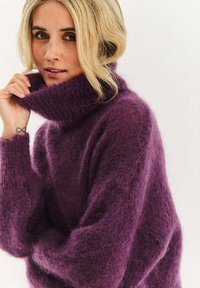 Fialový oversize rolákový sveter vyrobený z mäkkej, textúrovanej látky. Má vysoký golier a voľné rukávy, ktoré poskytujú pohodlný vzhľad.