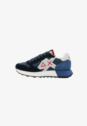 Zapatilla deportiva azul marino y blanca con símbolos geométricos rojos en el costado, talón de ante azul y suela blanca acolchada.