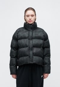 Čierna nafúknutá bunda s kratším strihom, obsahujúca prešívané sekcie a vysoký golier. Nepriamy maskáčový vzor a logo Nike na hrudi.