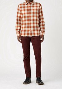 Rutig flanellskjorta i orange och kräm, långärmad, med knappstängning framtill, i kombination med bordeauxfärgade tajta byxor och svarta skor.