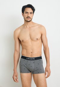 Gray cotton boxer briefs with a black waistband featuring the "LACOSTE" logo. The fabric has a subtle pattern of small logos.
