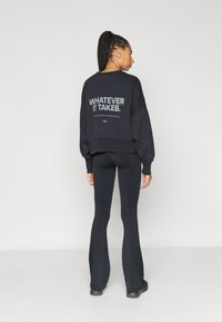 Μαύρο κοντό φούτερ με τη φράση «WHATEVER IT TAKES» στην πλάτη, σε συνδυασμό με μαύρο κολάν με καμπάνα και σκοτεινά υποδήματα.