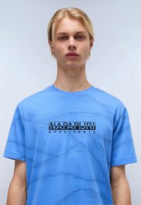 Maglietta in cotone blu con maniche corte, caratterizzata da un motivo testurizzato e il logo nero "NAPAPIJRI geographic" al centro.