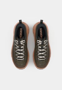 Sneakers Hoka One One w głębokim oliwkowym wierzchu, białych sznurówkach i teksturowanej brązowej podeszwie. Wyściółka wokół kostki i logo na języku.