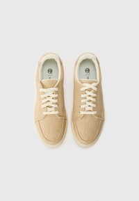 Beige kanvas sneakers med hvite snøringer, avrundet tå og myk kremfarget innside. Rent design med subtile sømmer og logo på innersålen.