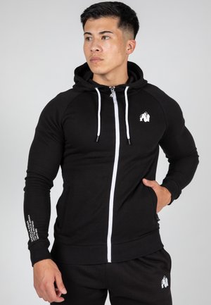 Schwarzer Zip-Hoodie mit weißen Kordeln und Logo. Verfügt über ein tailliertes Design, gerippte Bündchen und eine glatte Textur. Taschen an den Seiten.