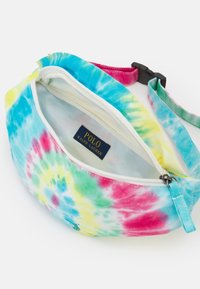 Saszetka biodrowa w tie-dye w odcieniach niebieskiego, różowego i żółtego, z białym zamkiem błyskawicznym i niebieską metką z napisem "POLO RALPH LAUREN". W zestawie regulowany pasek.