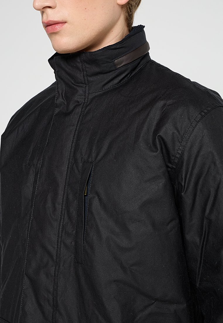 Veste noire imperméable avec col haut, poche zippée à l'avant et détails en cuir ; tissu texturé au design moderne.