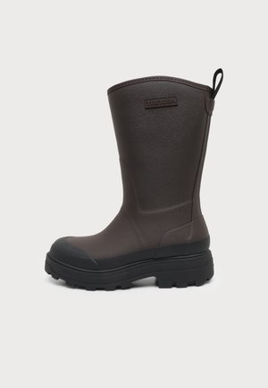 Botte en caoutchouc marron mi-mollet avec semelle noire épaisse, patte de tirage à l'arrière et logo "Tretorn" sur le côté extérieur près du haut.
