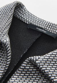 Gestructureerde kraag met een geometrisch patroon in zwart en wit, voorzien van een zachte zwarte voering en een "Someday." label.