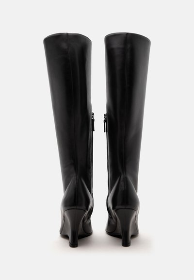 Paire de bottes hautes en cuir noir à talons, vues de dos avec fermetures éclair latérales et talons arrondis sur fond blanc.