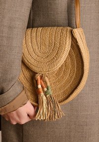 Borsa a tracolla intrecciata in paglia con design circolare, caratterizzata da frange colorate in arancione, verde e crema. Texture morbida e colore naturale.